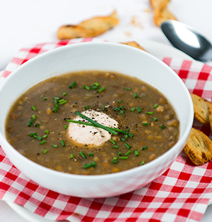 Lentil Soup with Chipotle Sauce made with Astro Yogurt served in a white soup bowl sitting on a red checked tablecloth with breadsticks on the side