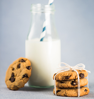 A stack of Nearly No Fat Peanut Butter Chocolate Chip Cookies made with Astro Yogurt next to a carafe of milk