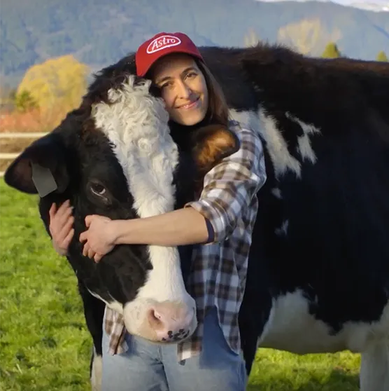 Woman hugging a cow wearing an Astro hat in a field