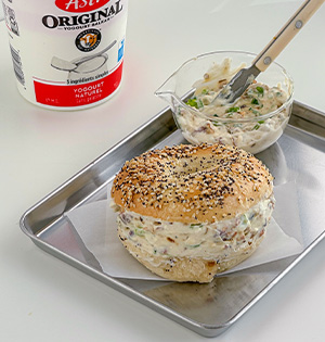 Bacon Scallion Yogurt Spread made with Astro Yogurt on a Bagel with an Astro Plain 6% Yogurt tub in the background.